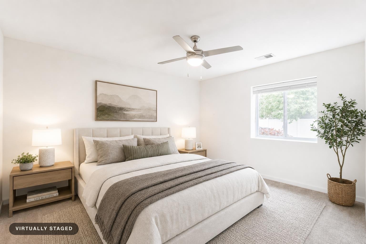 Modern bedroom with beige upholstered bed, gray throw blankets, two wooden nightstands with lamps, and a potted plant by the window.