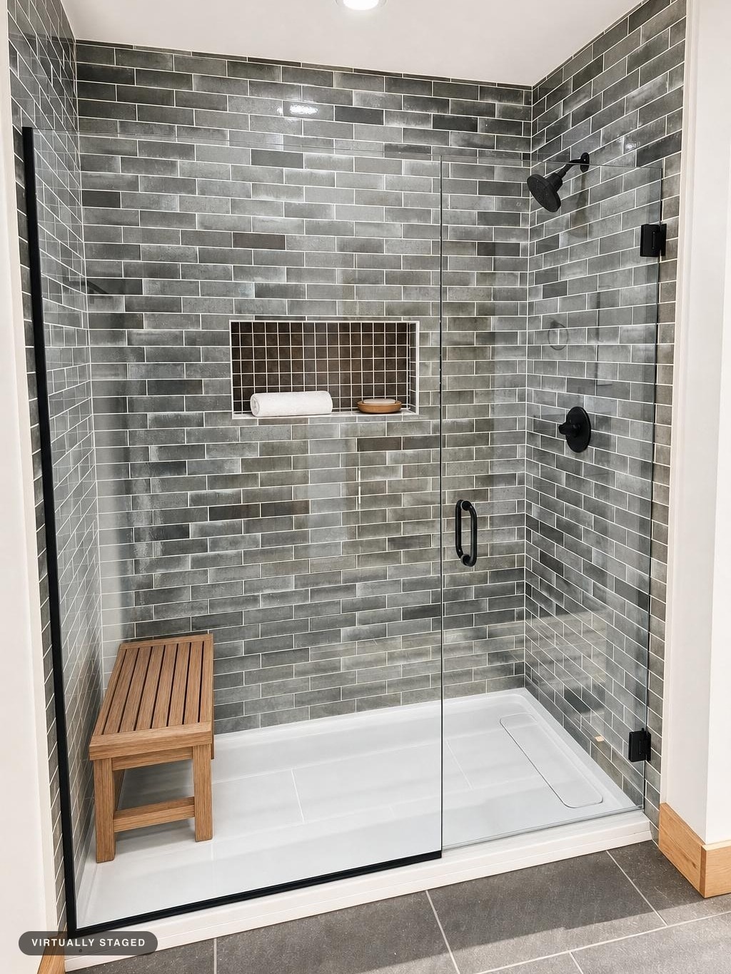 Glass-enclosed shower with gray subway tile walls, black shower fixtures, a wooden bench, and a recessed shelf with a towel and soap dish