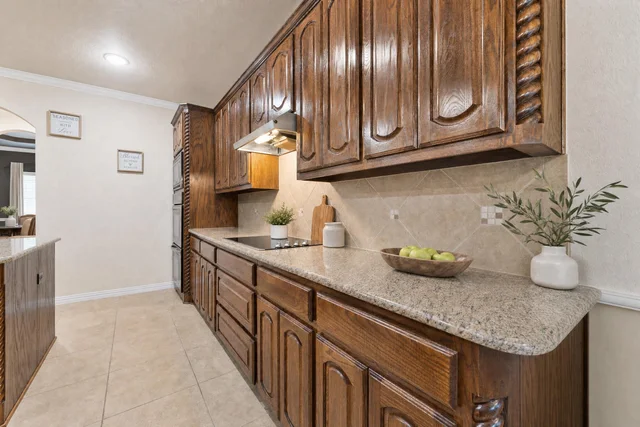 kitchen with dark wood cabinetry, granite look countertop, tiled backsplash, and light beige floor tiles