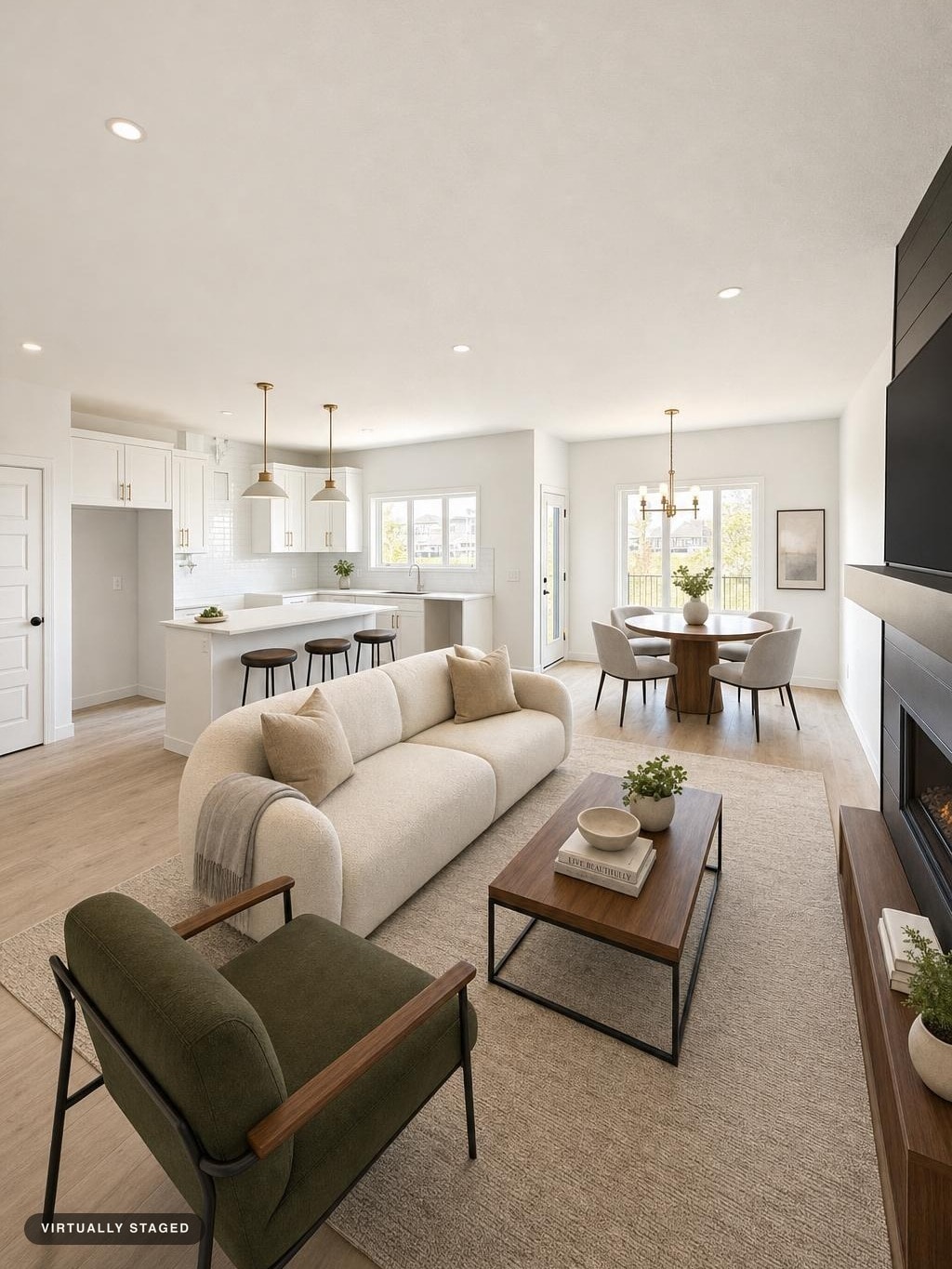 Modern living room with beige curved sofa, green armchair, wooden coffee table, and round dining table by large windows.