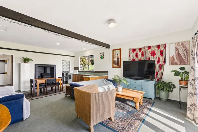 Living room with blue sofa, rattan chair, wooden coffee table, TV on a blue cabinet, and floral patterned curtains with sunlight.