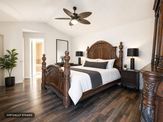 Traditional bedroom featuring a large carved wood bed with white linens and dark gray accents, flanked by nightstands and lamps.