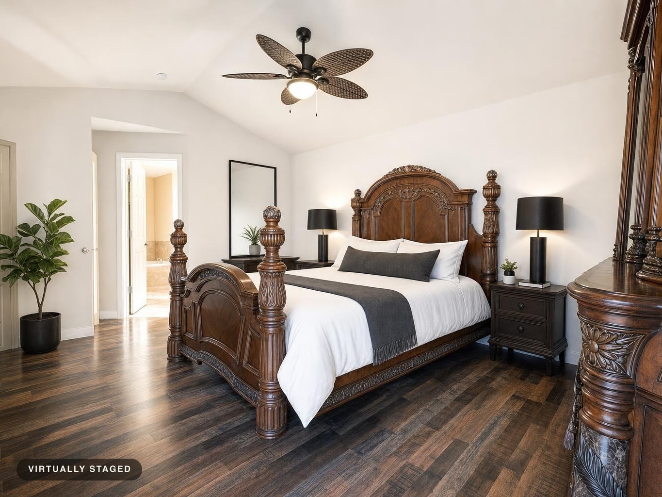 Traditional bedroom featuring a large carved wood bed with white linens and dark gray accents, flanked by nightstands and lamps.