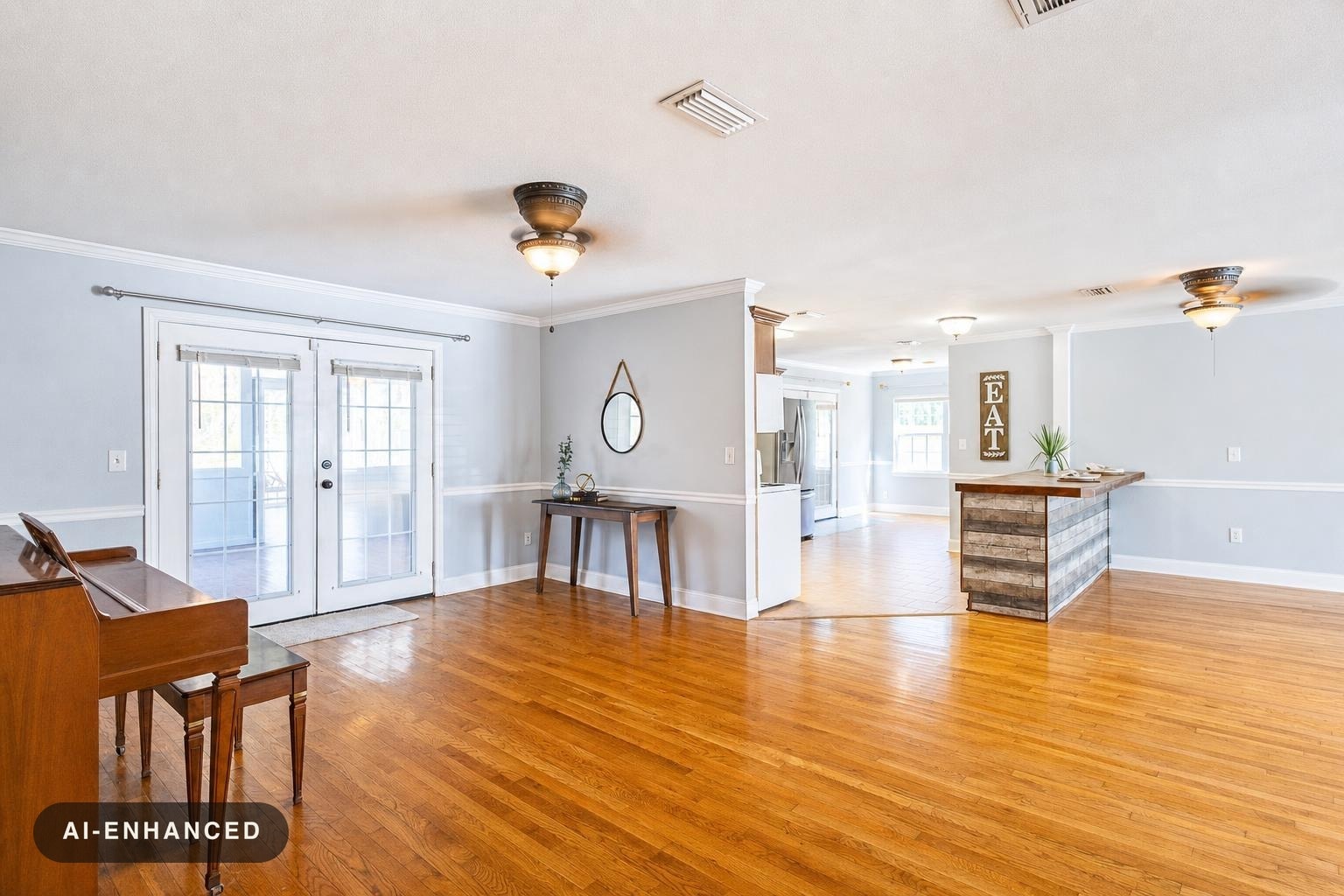 Modern living room with hardwood flooring, light gray walls, glass double doors, piano, console table with plant and round mirror.