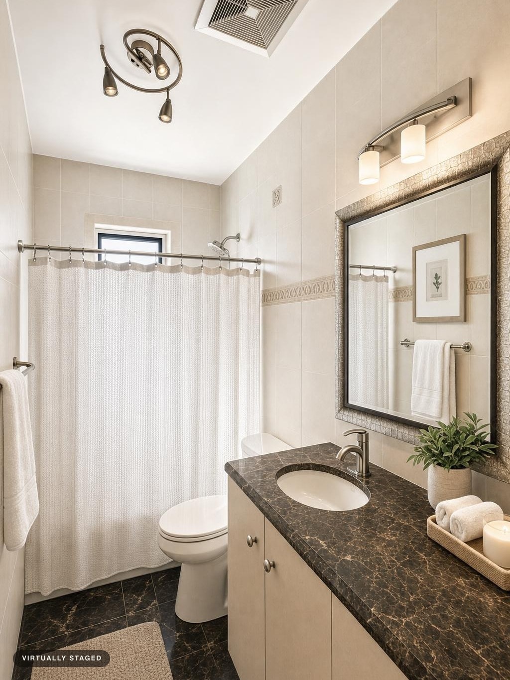 Small bathroom with beige tiled walls, dark marble countertop, white toilet, shower curtain, mirror, and light fixture.