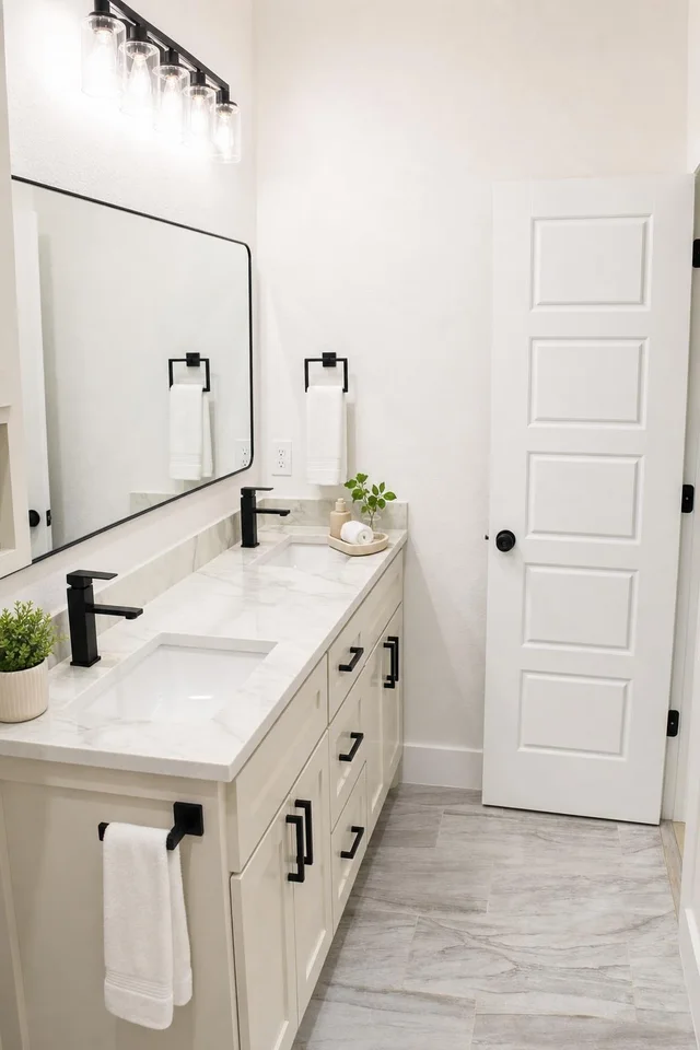 modern bathroom with white vanity, dual black faucets, large rectangular mirror, and light gray tile floor
