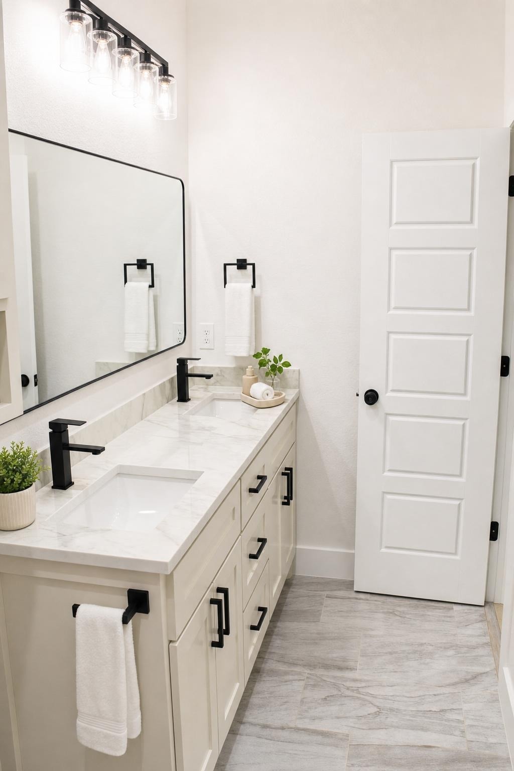 modern bathroom with white vanity, dual black faucets, large rectangular mirror, and light gray tile floor