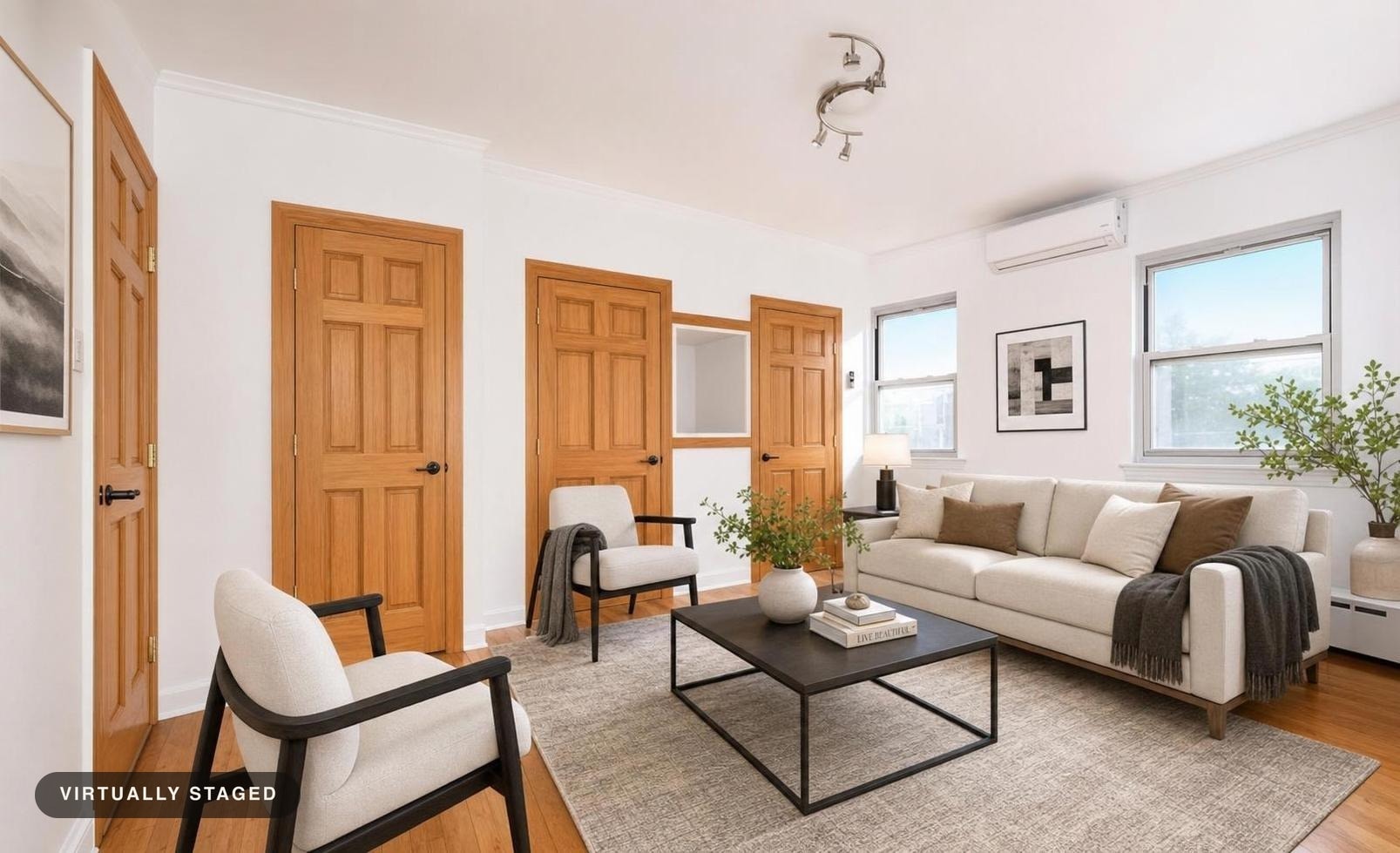 Modern living room with beige sofa, two light armchairs, black metal coffee table on gray rug, wood-paneled doors, and white walls.