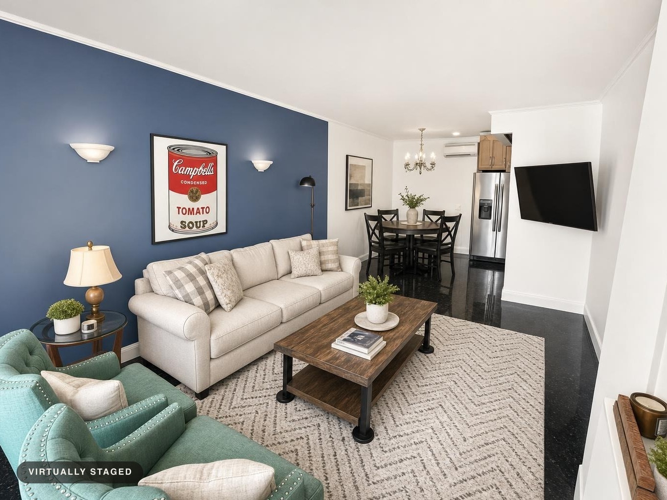 Living room with a beige sofa, teal armchair, wooden coffee table on a patterned rug, blue accent wall with wall sconces, and dining area in background.