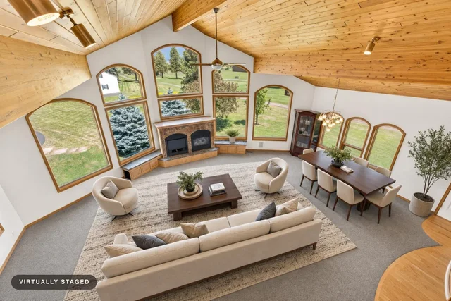 Modern living room with beige sofa, two round armchairs, wooden coffee table, dining set, and large arched windows showing greenery outside.