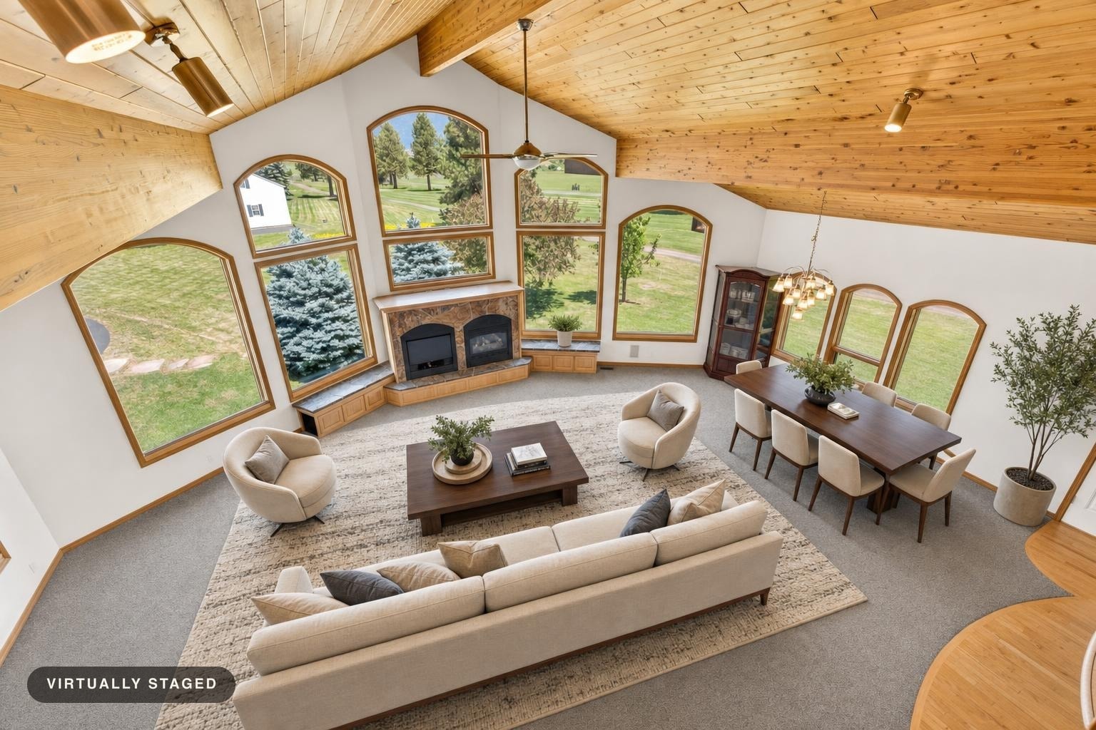 Modern living room with beige sofa, two round armchairs, wooden coffee table, dining set, and large arched windows showing greenery outside.