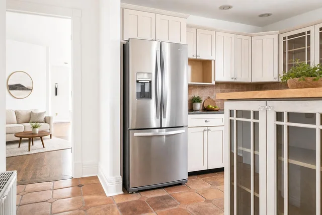 Bright kitchen with white cabinets, stainless steel French door refrigerator, and terracotta tile floor.