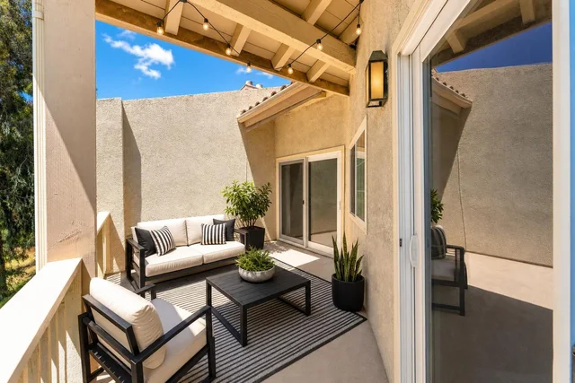Modern backyard patio with black metal-framed sofa and chair with beige cushions, a striped rug, black coffee table, and potted plants.