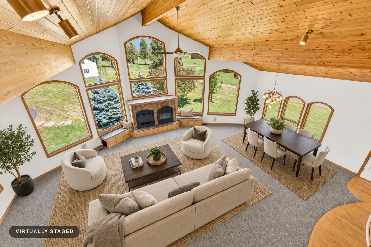 Luxury living room with vaulted wood ceiling, arched windows, stone fireplace, beige sofa, two swivel chairs, dark wood coffee table, and dining set.