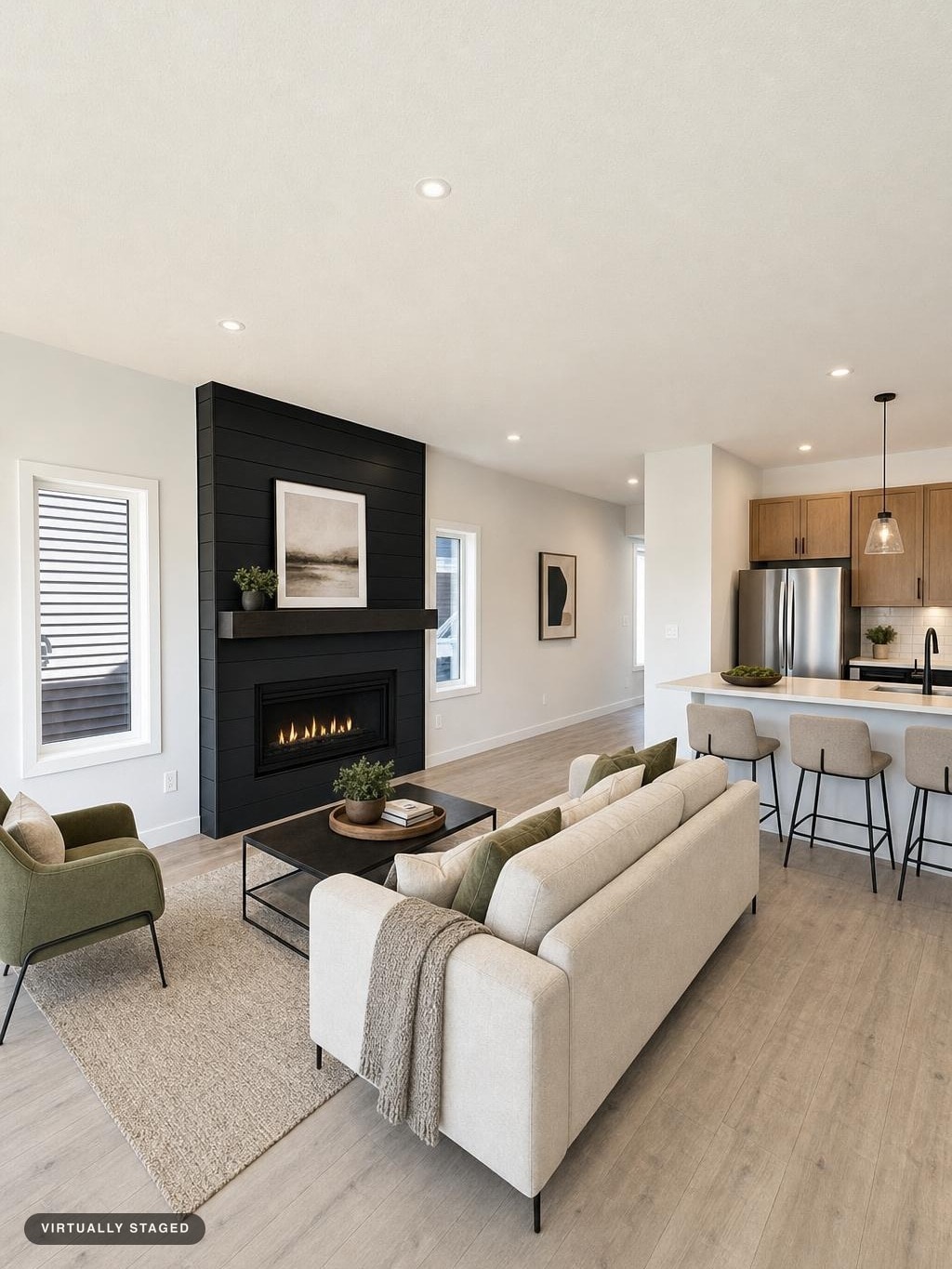 Modern living room with beige sofa, green armchair, black panel fireplace, coffee table, and kitchen bar stools.