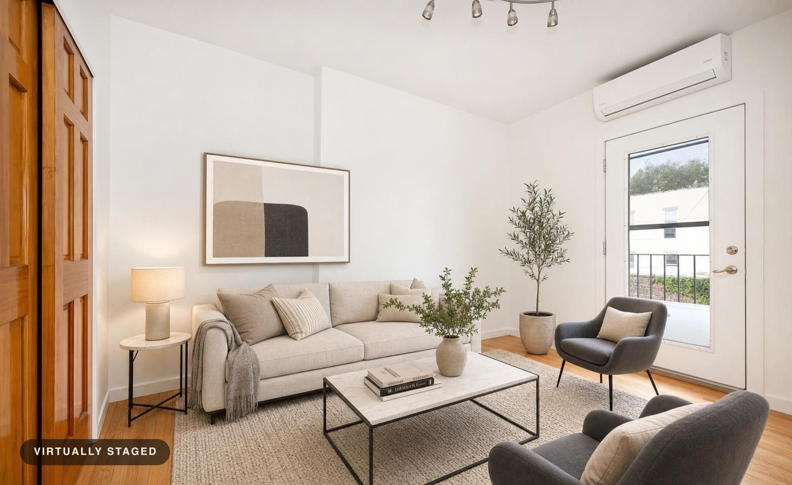 Modern living room with beige sofa, two black accent chairs, a light rug, two potted plants, a side table with lamp, and abstract wall art.