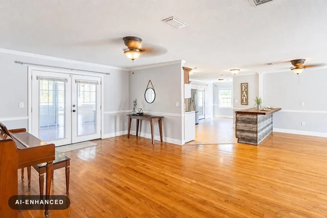 Spacious living room with wooden floor, piano on the left, small table with mirror on the wall, and kitchen island in the background.