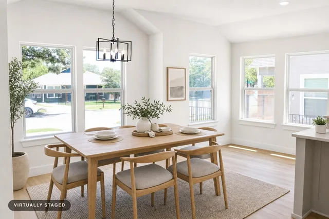 Scandinavian dining room with a light wood table, six matching chairs with gray cushions, and large windows letting in natural light.