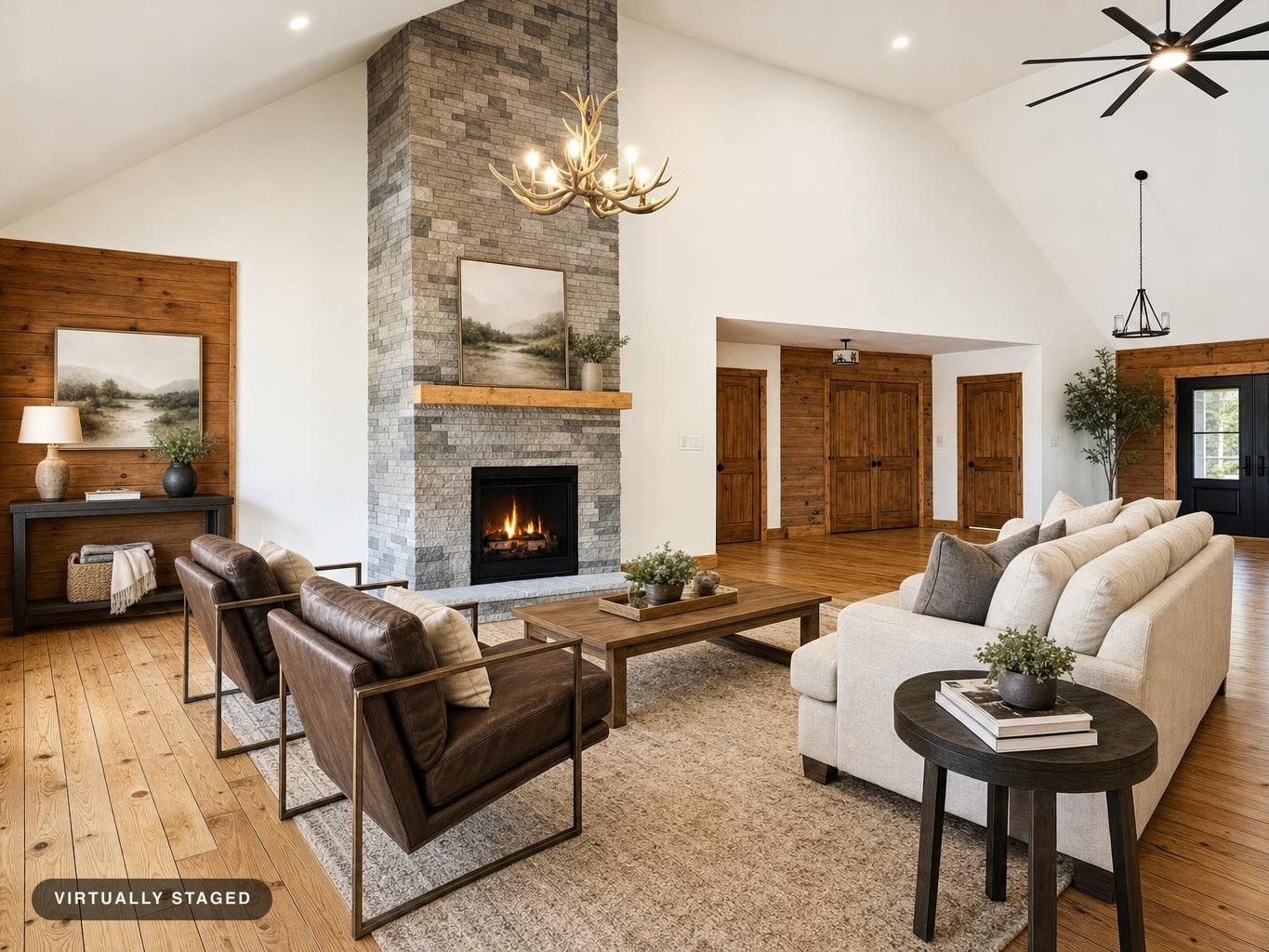 Spacious living room with stone fireplace, two brown leather armchairs, white sofa, and wood floors and accents.