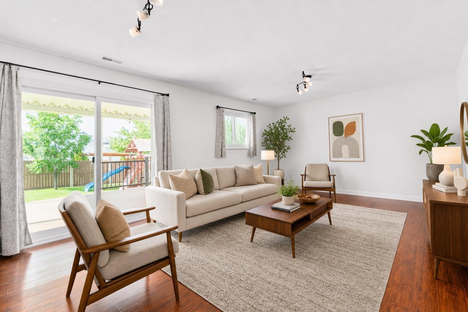Living room with beige sofa, two armchairs, wooden coffee table, large rug, and sliding glass door with garden view.