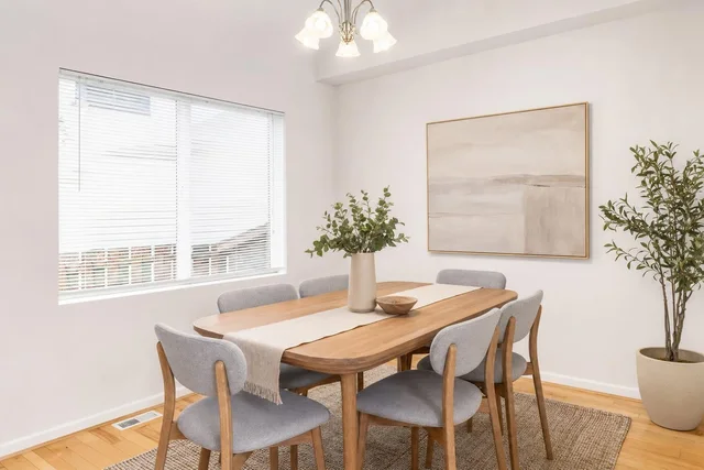 Scandinavian dining room with light wood table, six gray upholstered chairs, beige wall art, and large potted plant by window.