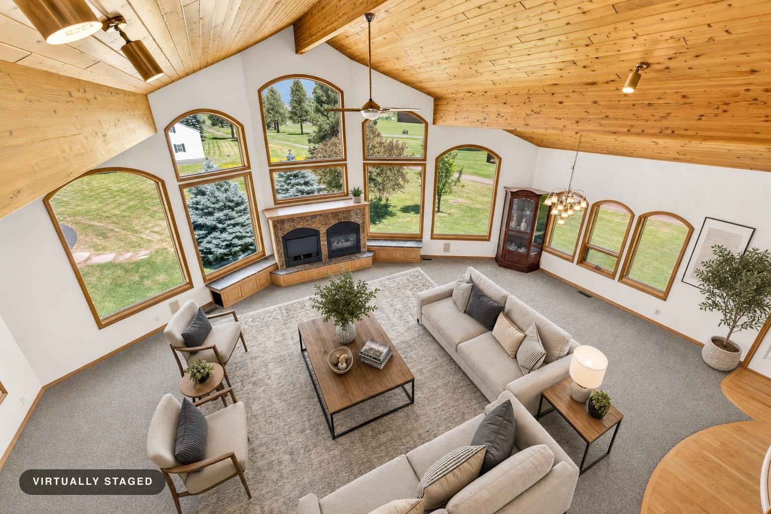 Spacious living room with wood vaulted ceiling, large arched windows, stone fireplace, two beige sofas, wooden coffee table, and accent chairs.