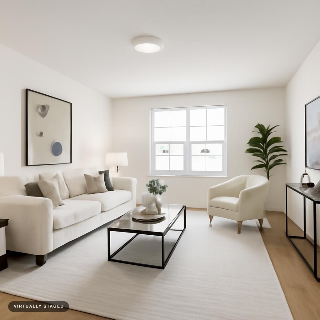 Bright modern living room with white sofa, armchair, black metal frame coffee table, light-colored rug, and plant near window.