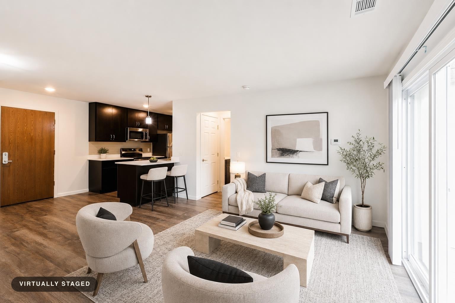 Modern living room featuring a beige sofa, two light gray armchairs with black pillows, light wooden coffee table, and large window to right.