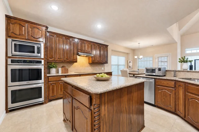 Traditional kitchen with warm wood cabinets, granite-look island countertop, and stainless steel built-in ovens and dishwasher.