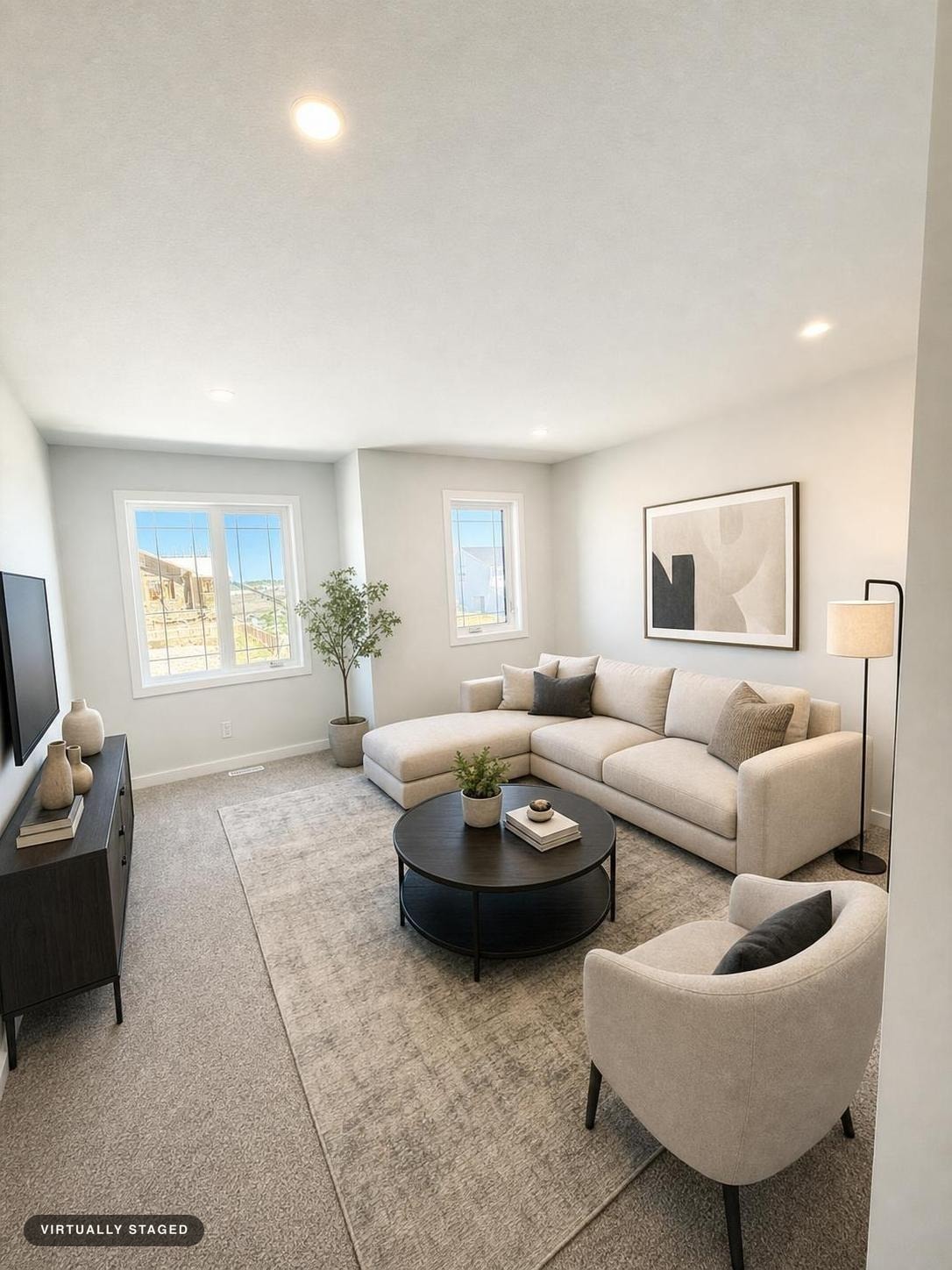 Bright modern living room with beige sectional sofa, round black coffee table, beige armchair, floor lamp, and abstract wall art.