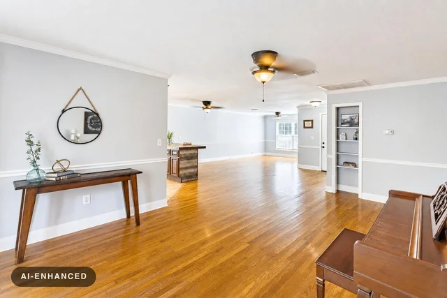 Spacious living room with wooden floor, light gray walls, a wooden console table with decor, a round mirror, and a brown piano.