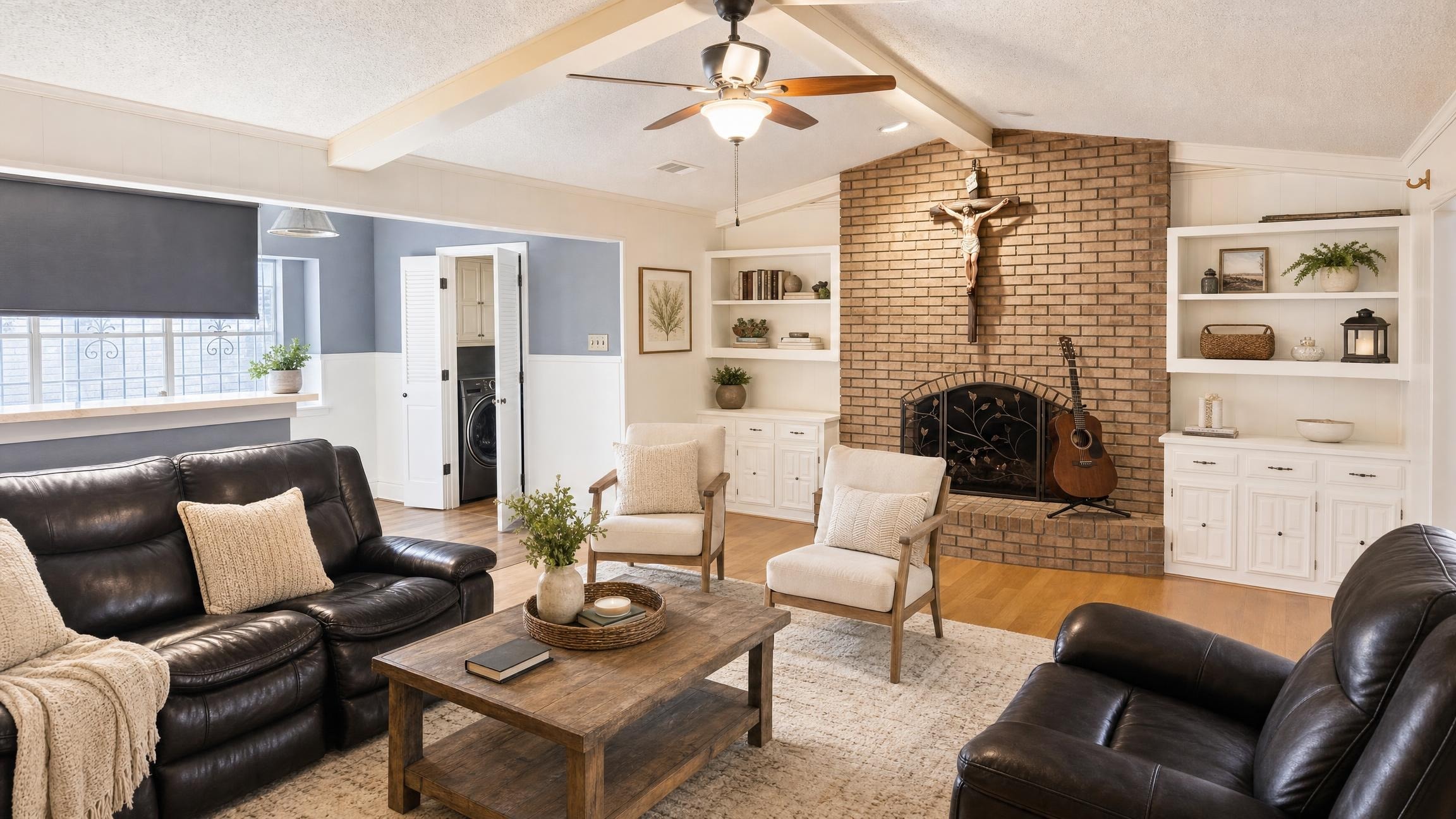 Farmhouse living room with brown leather sofas, wooden coffee table, two armchairs, brick fireplace, and ceiling fan.