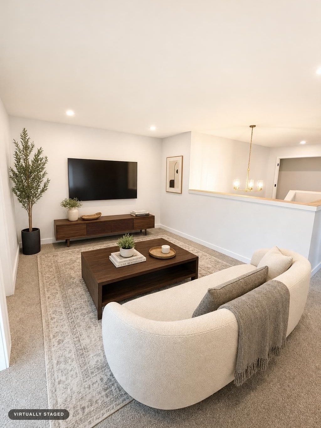 Modern living room with a curved beige sofa, wood coffee table, media console, and a large TV on a neutral patterned rug.