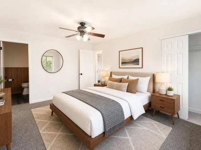 Midcentury bedroom with wood platform bed, white bedding, gray throw, beige rug, two nightstands with lamps, and round mirror on wall.