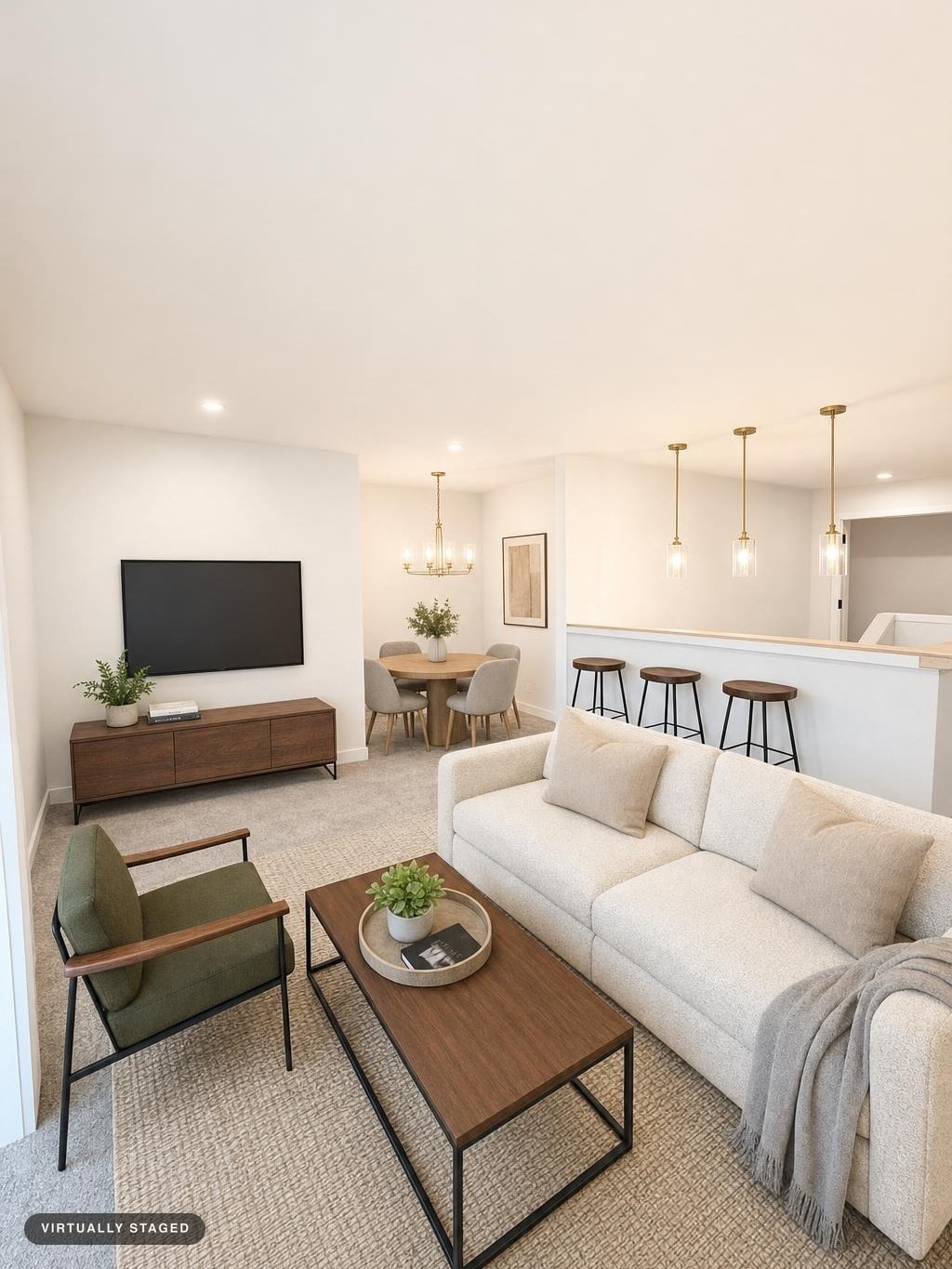 Bright living room with cream sofa, green armchair, wooden coffee table, wood media console, and dining area in background.