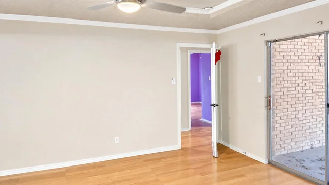Empty living room with beige walls, wooden floor, an open door, and a sliding glass door to outside.