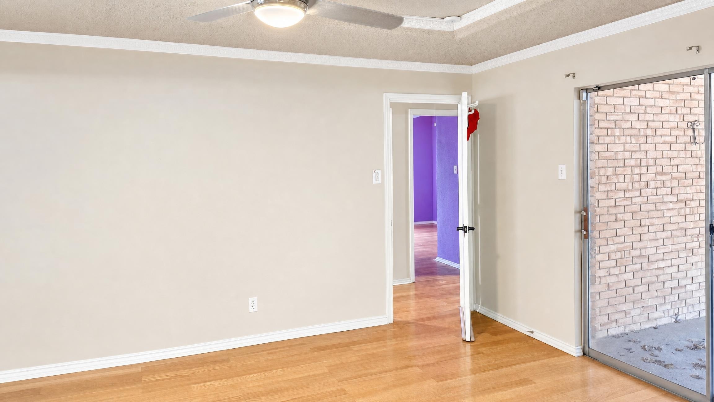 Empty living room with beige walls, wooden floor, an open door, and a sliding glass door to outside.