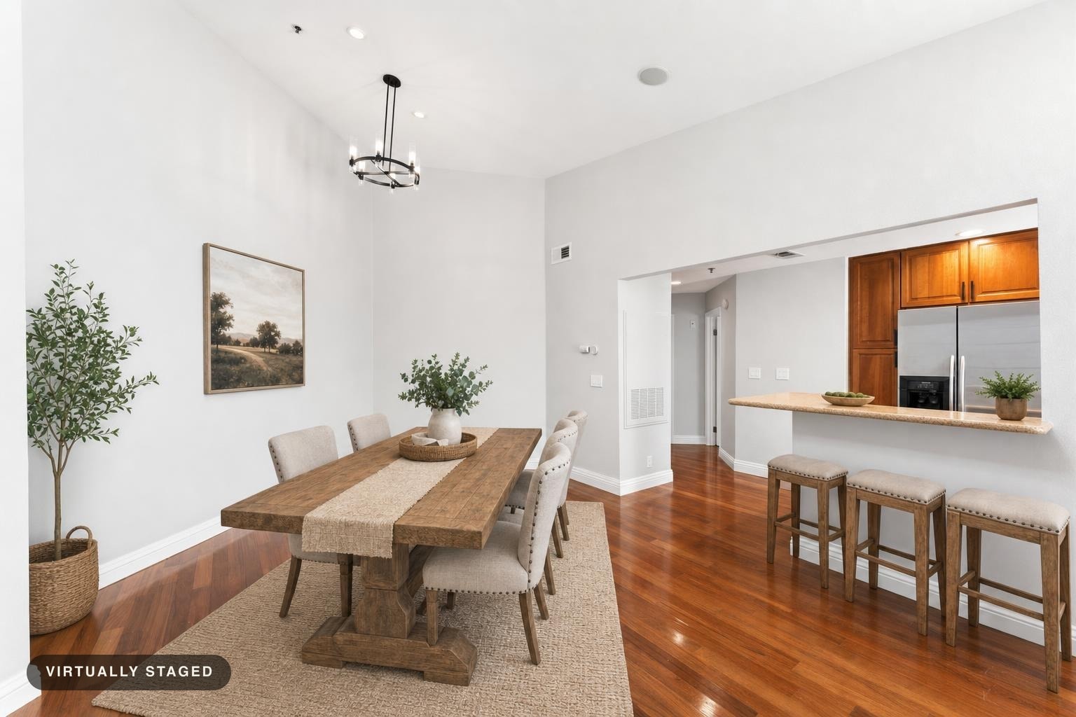 Dining room with wooden table, beige upholstered chairs, woven rug, and natural decor including a plant and wall art.