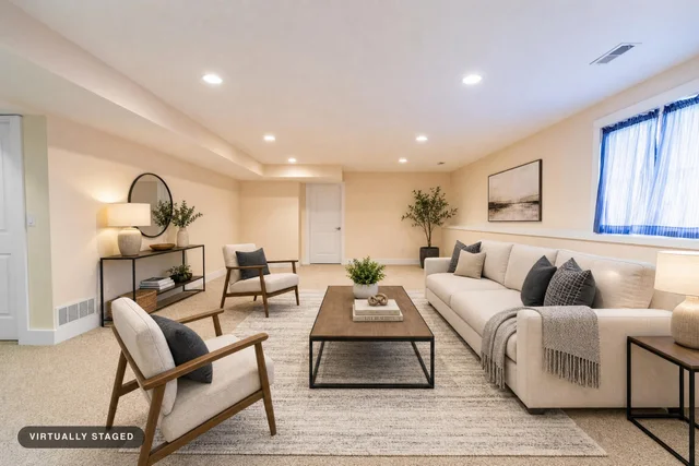 Modern living room with beige sofa, two armchairs, wood and metal coffee table, console and side tables, soft rug, and neutral decor.