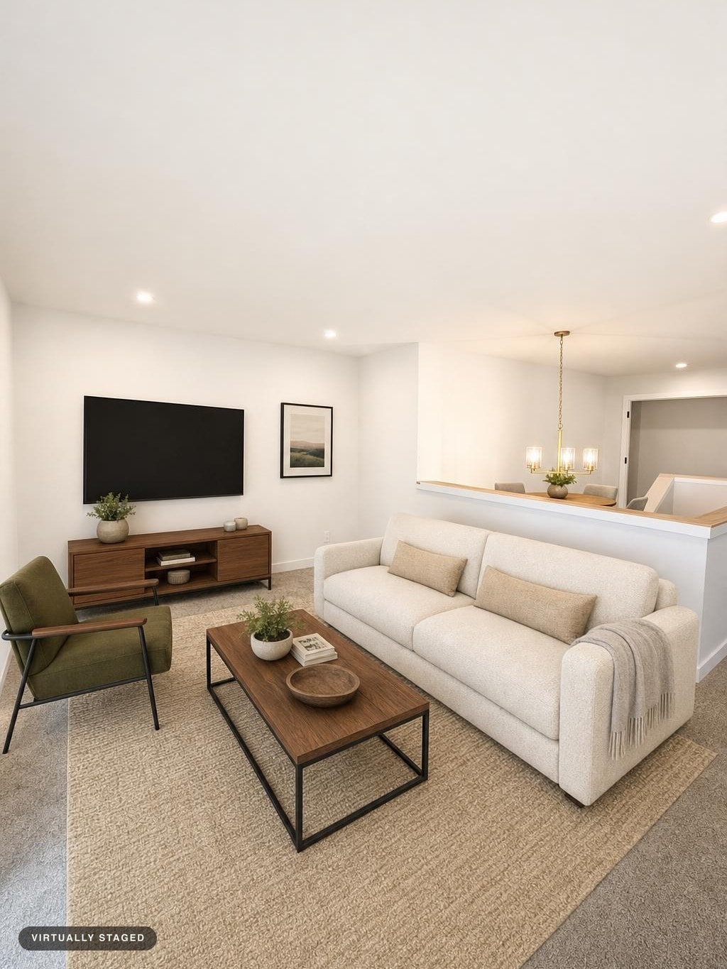 Modern living room with beige sofa, olive green armchair, wooden coffee table, and wooden media console beneath a wall-mounted TV.