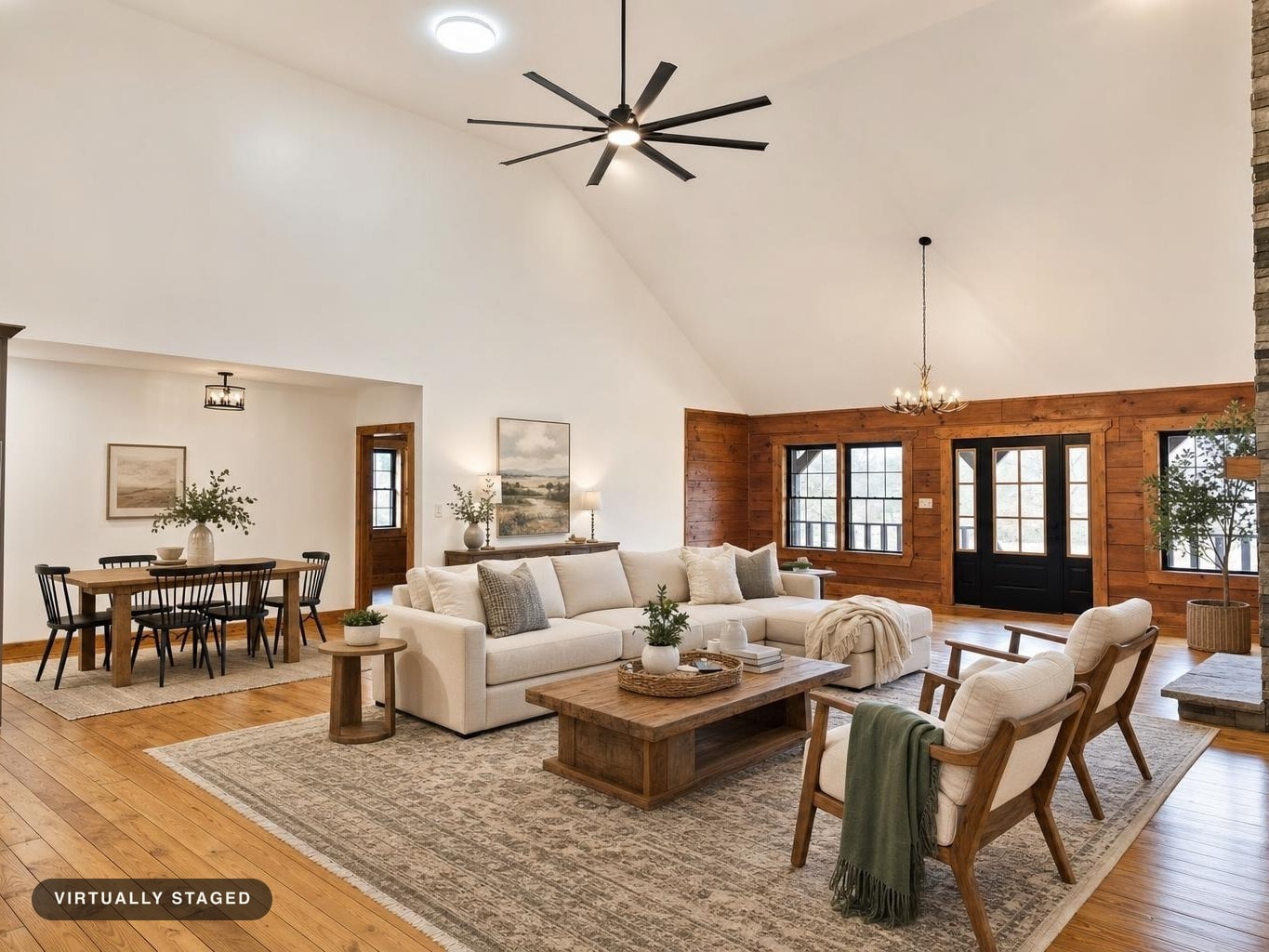 Living room with vaulted ceiling, white sofa, wooden coffee table, two beige armchairs, and black door with windows.