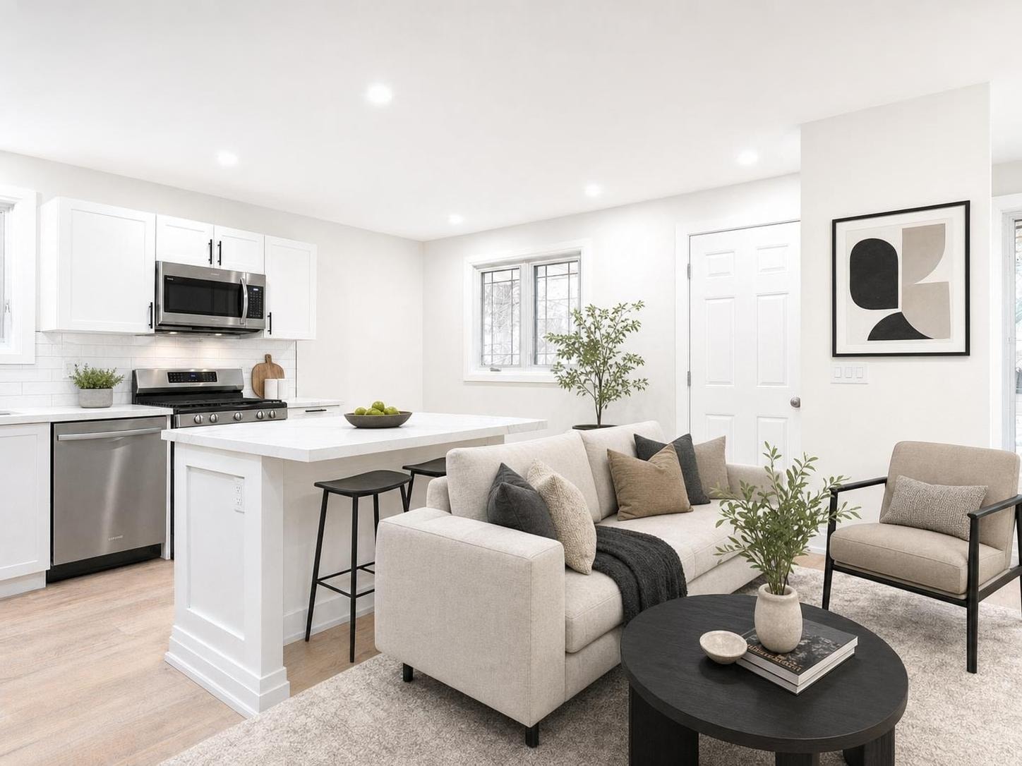 Modern living room with beige sofa, black armchair, black coffee table, and white kitchen island under soft lighting.