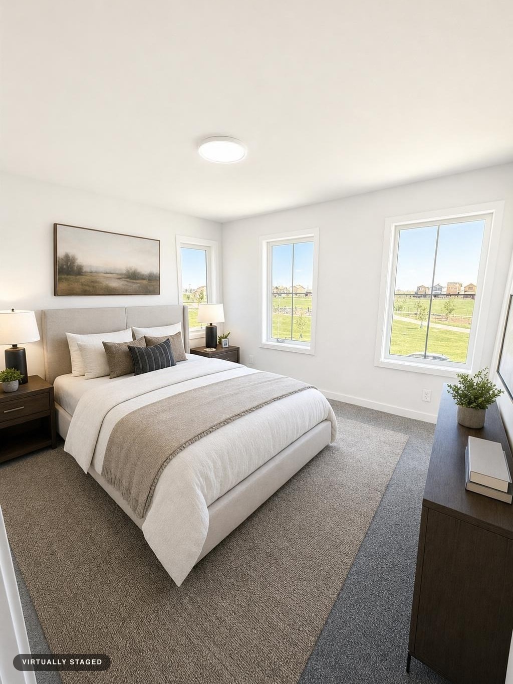 Bright modern bedroom with an upholstered bed, two nightstands, two lamps, artwork above bed, and dresser under window.