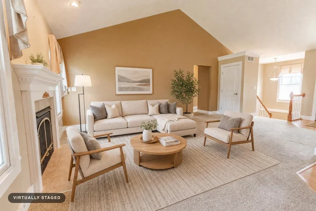 Living room with beige walls, light wood-framed sofa and chairs, round wood coffee table, and floor lamp near fireplace.