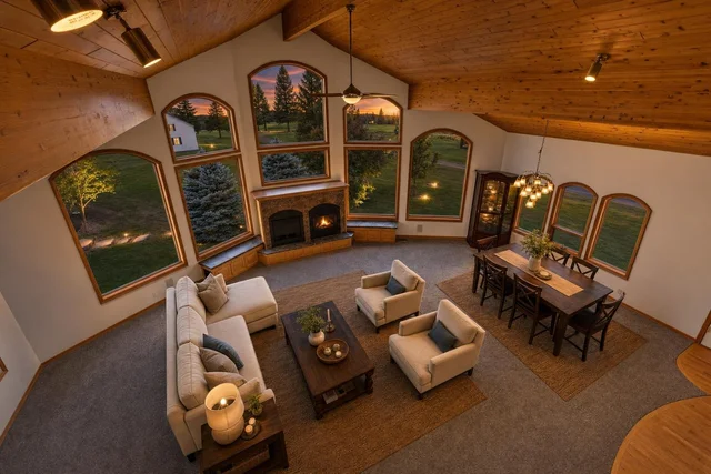 Living room with vaulted wood ceiling, large arched windows, beige sofa set, wooden coffee table, dining area, and fireplace.