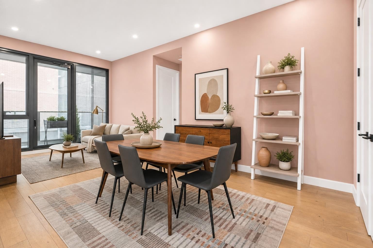 Modern living and dining space with wooden floor, medium wood table, leather-look chairs, beige sofa, and pink walls.