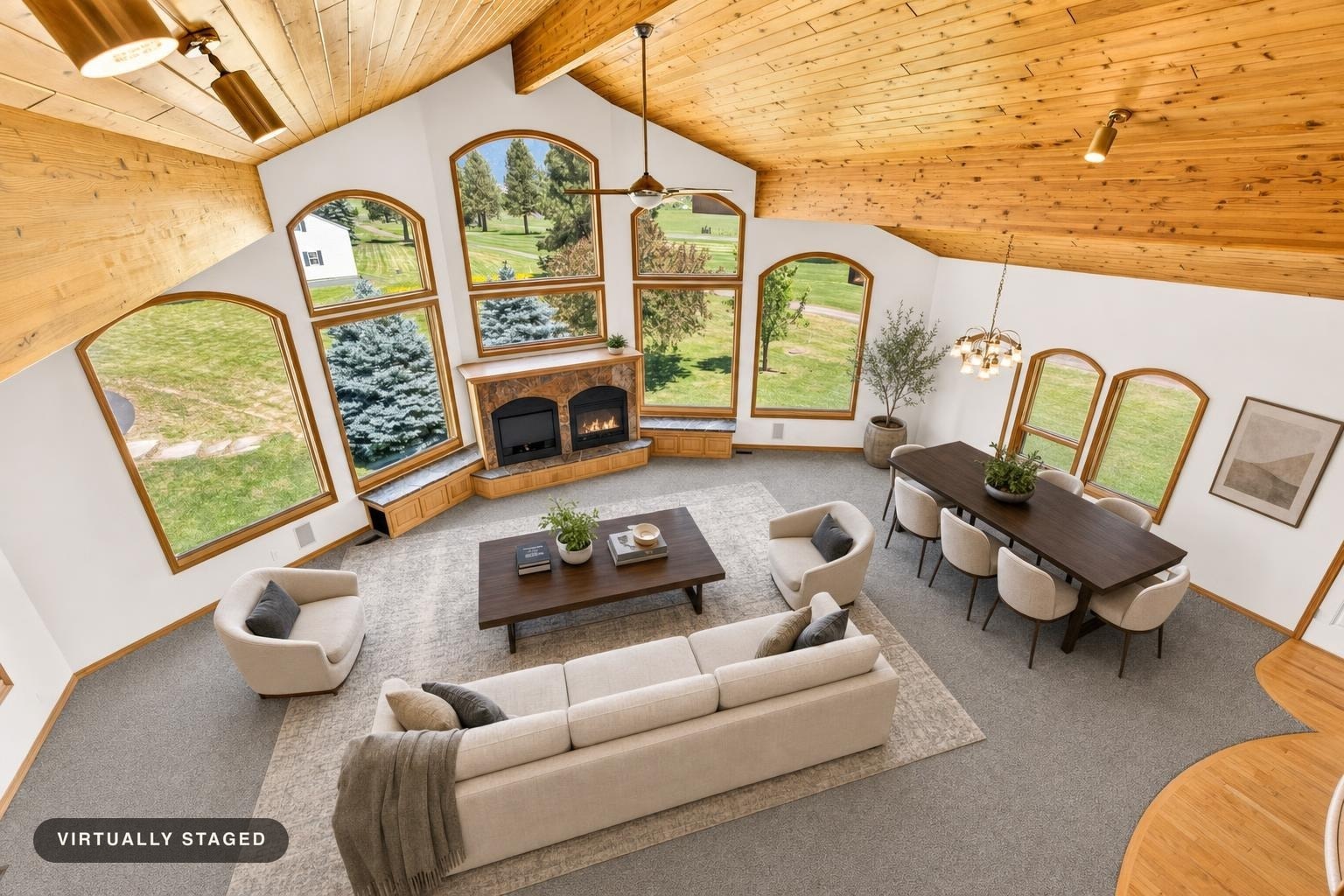 High-ceiling living room with large arched windows, beige sectional sofa, two armchairs, dark wood coffee and dining tables, and gray carpet.