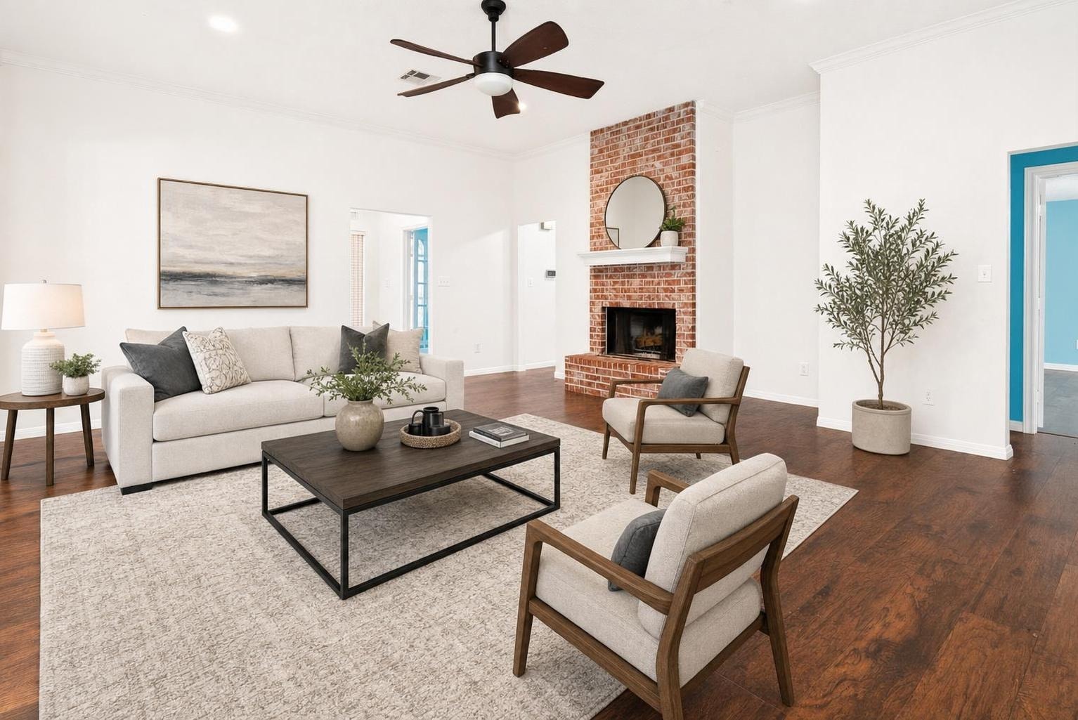 Bright modern living room with beige sofa, two armchairs, dark wood coffee table, brick fireplace, and wood flooring.