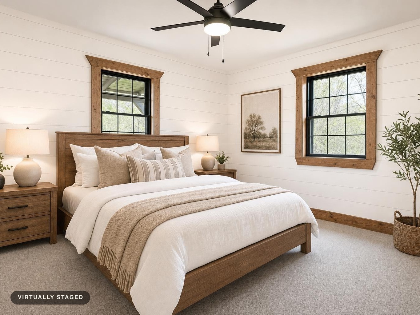 Bedroom with wood bed frame, matching nightstands with lamps, neutral bedding, two windows with wood trim, a framed tree art, and a potted plant.
