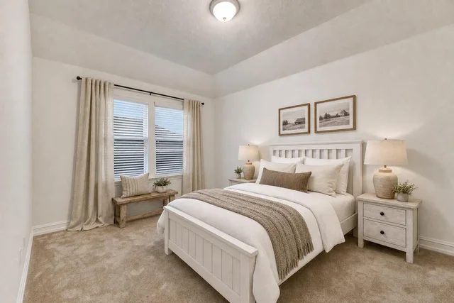 Farmhouse-style bedroom with white wooden bed, beige lamps on nightstands, beige curtains, and a wooden bench under a window.